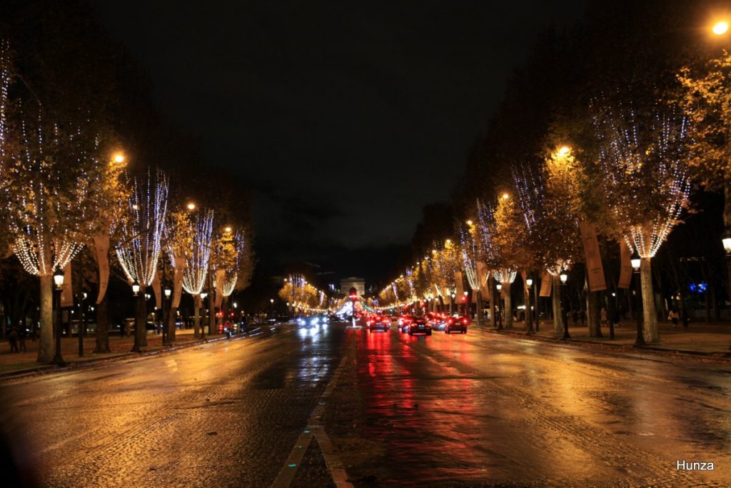 Champs-Elysées illuminées pour les fêtes de Noël, avec rangées d’arbres décorés et circulation nocturne