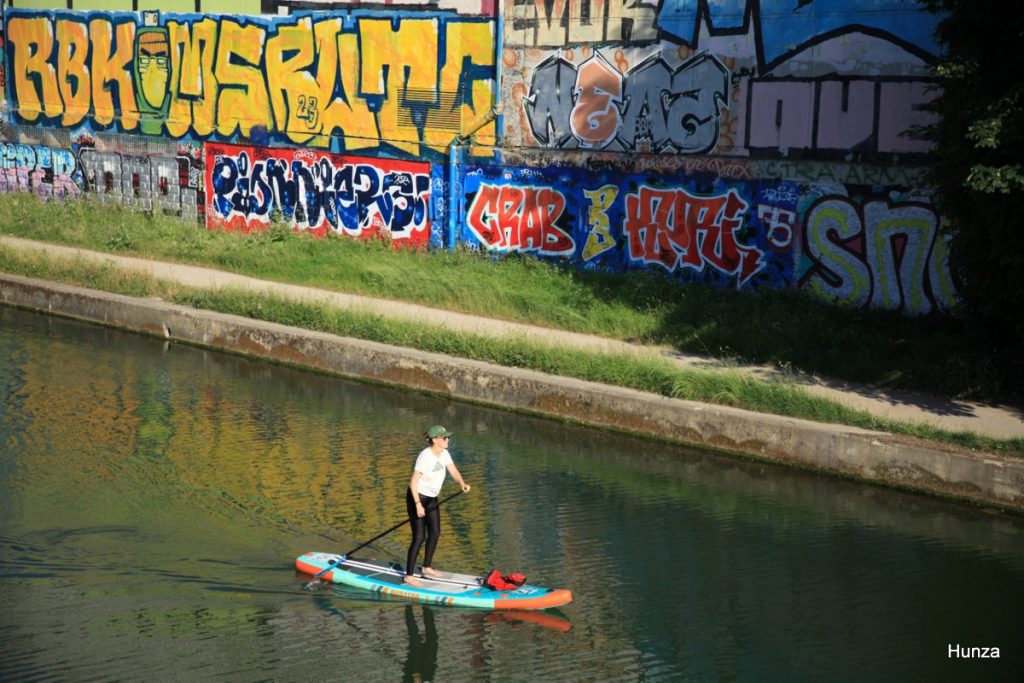 Pratiquante de paddle sur le canal de l'Ourcq devant des fresques de street art à Bobigny