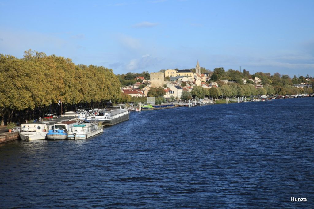 Vue de Conflans-Sainte-Honorine depuis la passerelle Saint-Nicolas, avec les bateaux amarrés sur la Seine et le centre ancien en hauteur.